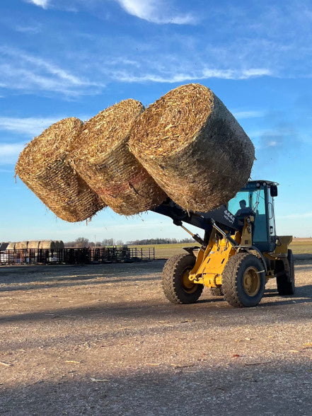 Durable 5XD Bale Spear lifting a heavy round bale onto a trailer during farm loading operations.