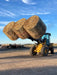 Durable 5XD Bale Spear lifting a heavy round bale onto a trailer during farm loading operations.