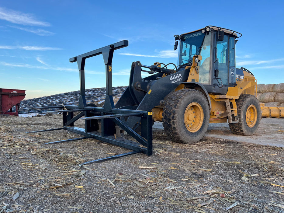 Farmer using the Series 5XD Bale Spear to stack round hay bales neatly inside a barn.