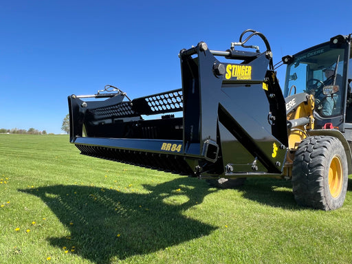 Heavy-duty tractor rock bucket attachment lifting large stones and debris during land clearing operations.