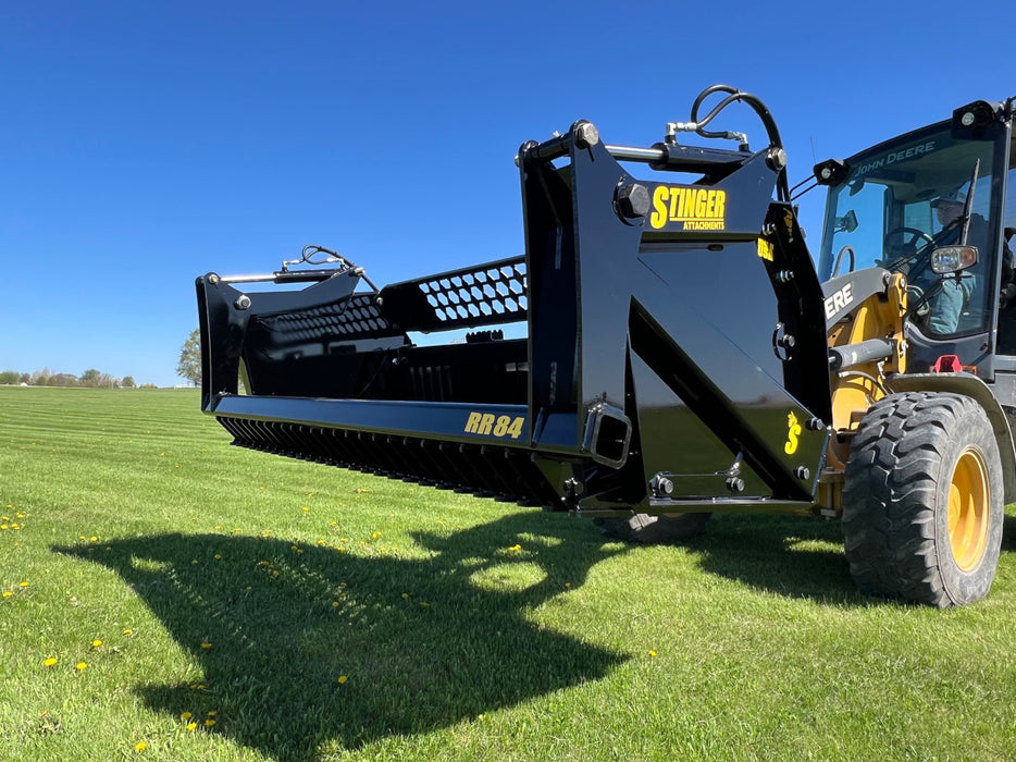 Heavy-duty tractor rock bucket attachment lifting large stones and debris during land clearing operations.