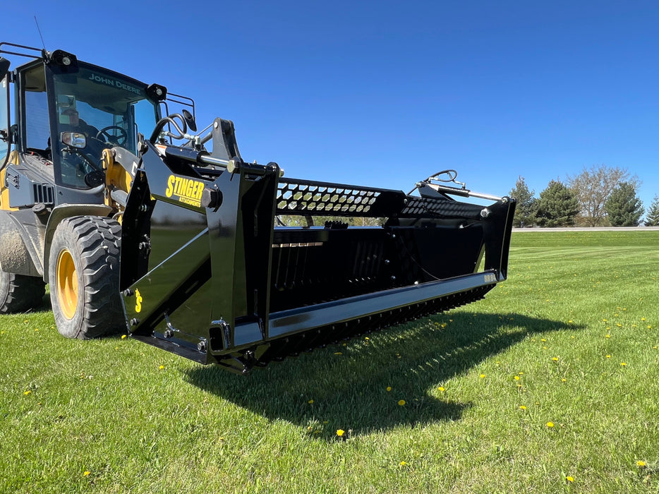 Operator using a tractor rock bucket to separate rocks from topsoil on rugged terrain.
