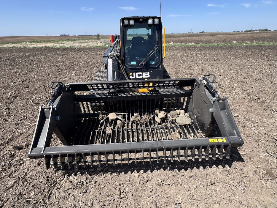 Operator using skid steer rock reel to sift rocks from soil – efficient attachment designed for grading, sorting, and land preparation.