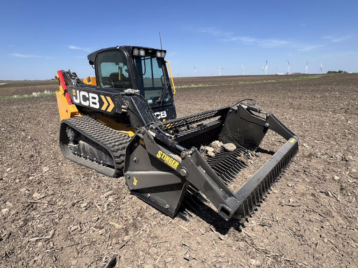 Heavy-duty skid steer rock reel attachment collecting rocks and debris – durable design engineered for efficient land clearing and cleanup.