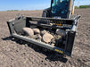 Rear perspective of a tractor rock bucket connected to a front loader with quick-attach system visible.