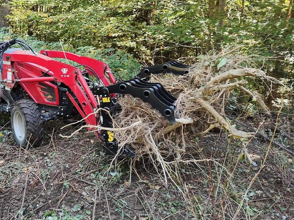 Compact tractor grapple bucket by Stinger in action clearing brush – powerful, versatile attachment for lifting, gripping, and transporting materials.